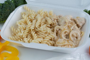 Beyaz bir beslenme çantasında, haşlanmış makarna ve kremalı tavuk. Fast food konsepti, paket yemek, yemek teslimatı..