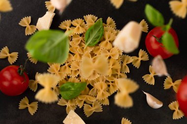 Uçan domateslerin bulanık görüntüsü, makarna, sarımsak karanfilleri, koyu arkaplanda fesleğen.