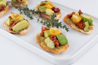 Beyaz tabakta pesto soslu bruschetta, güneşte kurutulmuş ve taze domates, avokado. Fotoğraf: Bokeh efektli.