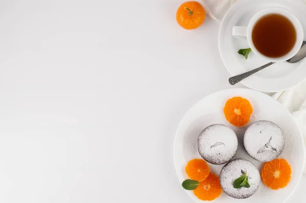 Plate with muffins, tangerines, mint leaves, a cup of tea on a white background with space for writing text.High-calorie food concept.