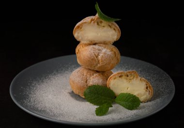 Koyu arkaplandaki eklerin bulanık görüntüsü, gri bir tabakta nane yapraklarıyla pudra şekeri serpiştirilmiş. Ekmeklerden biri kırılmış..