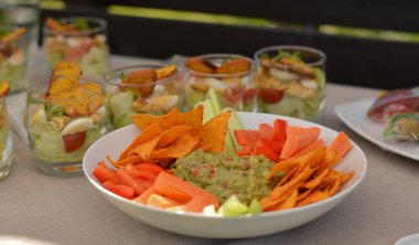 Önde sebzeli guacamole ve beyaz tabakta nachos, arkada cam tabaklarda salatalar....