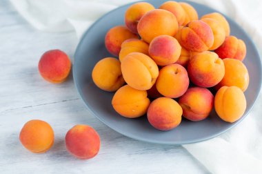 Hafif bir arka planda, olgun, sulu kayısılarla dolu beyaz bir tabak..