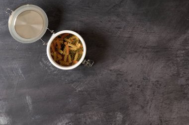 Beyaz seramik bir kavanozun ayrıntıları. Arka planda İtalyan makarna sarmalı ve hava geçirmez kapaklı.