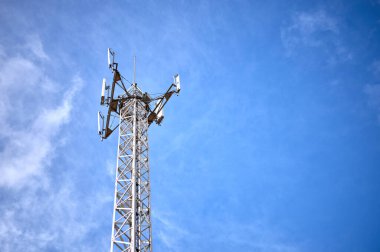 Mavi ve bulutlu bir gökyüzü üzerinde telefon, radyo ve televizyon iletişim antenleri olan metalik bir kule detayları