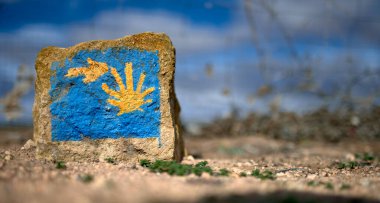detail of a milestone representing the sign of the Way of St. James with an arrow and a yellow shell on a blue background clipart