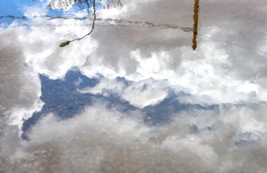 Mavi gökyüzündeki bir su birikintisindeki yansımanın ayrıntıları, bulutlar ve bazı sokak lambaları