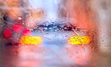 Önünde ışıklar açık araçlar olan bir arabanın camındaki yağmur damlalarının ayrıntıları