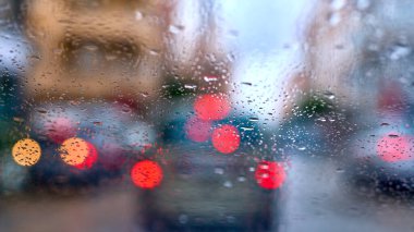 Önünde ışıklar açık araçlar olan bir arabanın camındaki yağmur damlalarının ayrıntıları