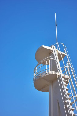 Mavi arka planda metal parmaklıkları olan beyaz beton bir gözetleme kulesinin detayları