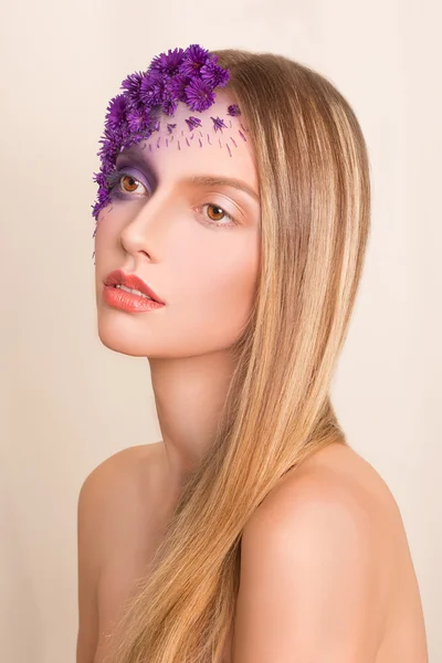 Retrato de una joven hermosa chica fresca con un maquillaje elegante y flores púrpuras alrededor de su cara y cabello . — Foto de Stock