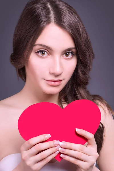 Modelo sexy Retrato de mujer. Preciosa joven morena con almohada roja en forma de corazón. Maquillaje perfecto. Un beso. Día de San Valentín morena dama headshot — Foto de Stock