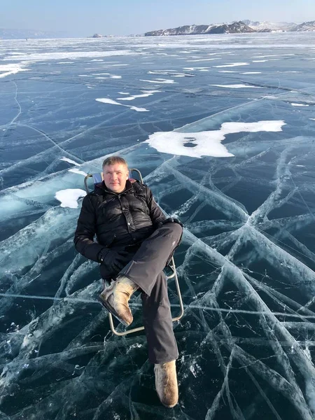 Турист, сидящий на поверхности трещин замерзшего озера Байкал в зимний сезон в Сибири, Россия. Байкал - самое большое пресноводное озеро в мире и самое глубокое озеро в мире. — стоковое фото