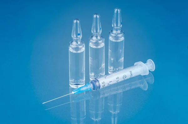 Coronavirus aşısı: mavi arka planda şişeler ve şırınga enjeksiyonu, COVID-19 'dan korunma, aşılama ve tedavi için kullanılır.