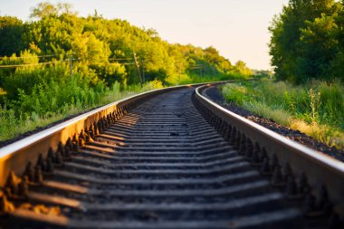 Demiryolunun fotoğrafı, yaz günbatımında yeşilliğin arka planına doğru gidiyor.