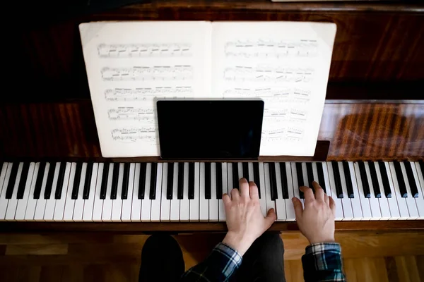 Teacher playing piano during online lessons using a tablet to communicate with his students