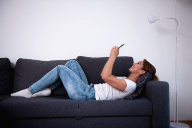 Oturma odasında akıllı telefonunu kullanan güzel bir kadın.