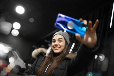 Şehir ışıklarında selfie çeken bir kadın.