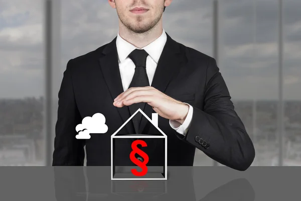 Businessman holding protective hand above building paragraph sym — Stock Photo, Image