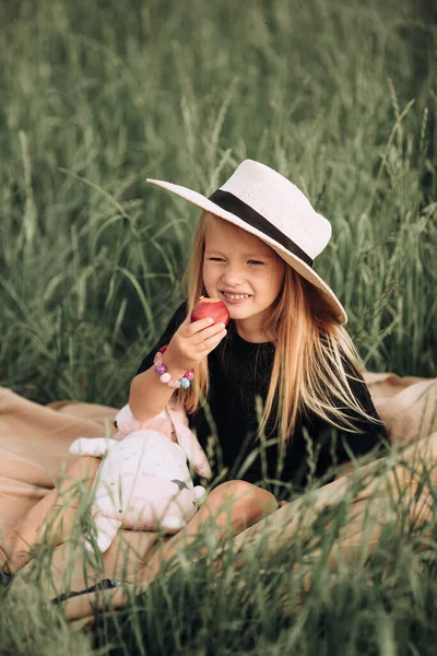 실외 피크닉에 붉은 복숭아를 손에 들고 짚 모자를 쓴 미소짓는 어린 소녀의 모습 행복 한 여름날의 개념 — 스톡 사진