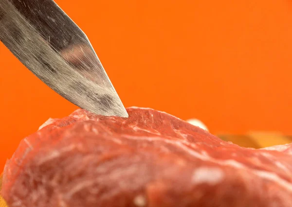 Close-up shot of a butcher\'s knife and a piece of red raw pork meat on a bright orange background. Butcher\'s shop. Meat cutting knives, selective focus, shallow depth of field