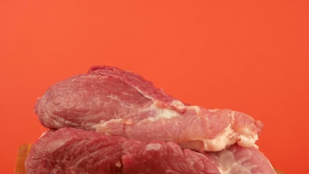 Ostrý velký řeznický nůž se zabodne do syrového červeného masa. Kousky čerstvého vepřového a nůž na jasně oranžovém pozadí. Téma vaření masa a masných výrobků. Klobása. Selektivní zaměření