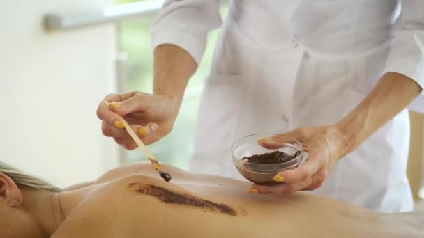 Blonde se trouve dans un salon de soins spa et est enduite d'argile cosmétique sur le dos. Rajeunissement de la peau et santé, relaxation — Video