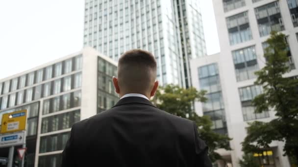 Un joven y brutal hombre de negocios con traje salió de la oficina mirando rascacielos y esperando una reunión con un cliente. — Vídeos de Stock
