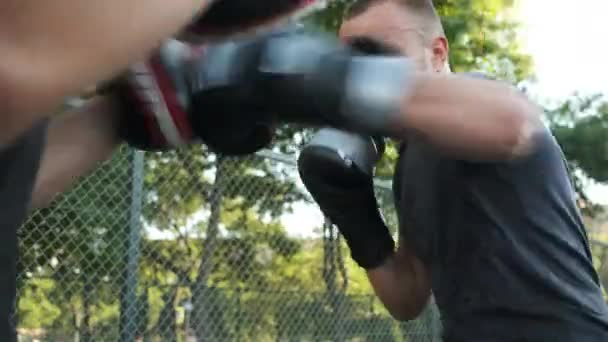 Boxeo. Un joven de apariencia caucásica entrena con su entrenador en la calle. Deportes y salud — Vídeo de stock