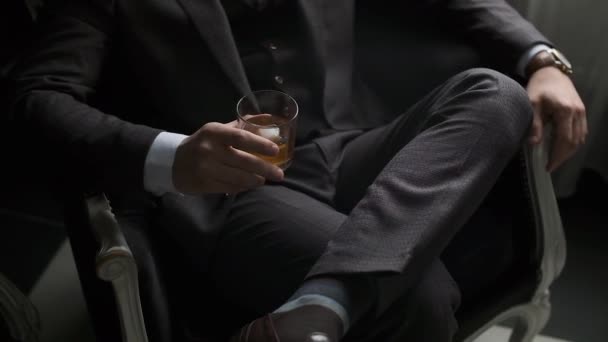 L'uomo elegante in una tuta si siede sul divano e tiene un bicchiere di alcol. Riflessione delle idee. Depressione e rilassamento — Video Stock