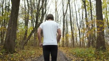 Genç sakallı bir adam parkta koşar ve müzik dinler. Sonbahar parkında spor ve sağlık