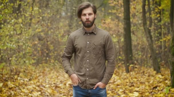 A brutal bearded Caucasian man standing in an autumn park looking at the camera and straightening his hair. Self-isolation during an epidemic — Stock Video