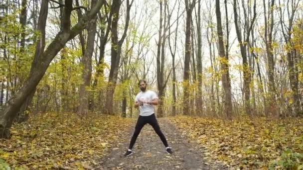 Atleta com fones de ouvido verdes ouve música no parque e aquece antes de correr. Esportes e saúde — Vídeo de Stock