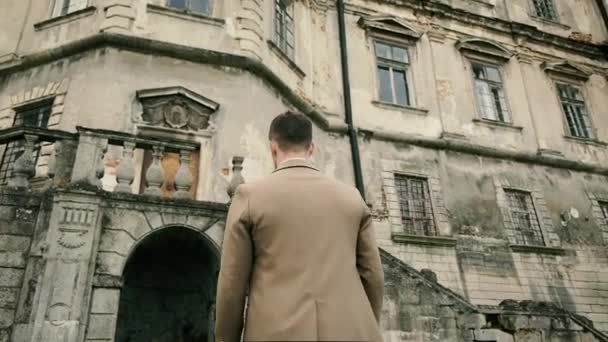 Homem caucasiano elegante em um terno marrom caminha perto do castelo. Moldura por trás. Depressão e reflexão de ideias — Vídeo de Stock