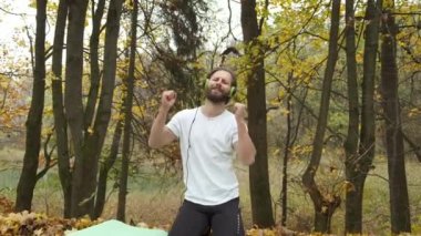 Sakallı beyaz bir adam sonbahar parkında bir minderin üzerinde oturur ve duygusal olarak müzik dinler. Mutlu ve neşeli kişi