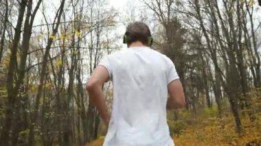 Genç sakallı bir adam parkta koşar ve müzik dinler. Sonbahar parkında spor ve sağlık. Arkadan portre çerçevesi