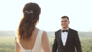 Takım elbiseli damat geline yaklaşır ve çiçekleri verir. Dağların ve nehrin arka planında mutlu bir düğün