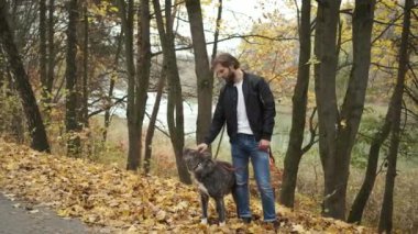 Sonbahar parkında köpeği gezdiren beyaz bir adam. Köpeği sev ve ona bak.