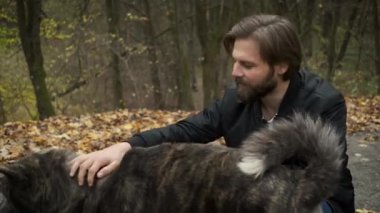 Sonbahar parkında köpeği gezdiren beyaz bir adam. Köpeği sev ve ona bak.