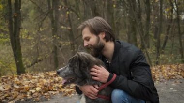 Sonbahar parkında köpeği gezdiren beyaz bir adam. Köpeği sev ve ona bak.