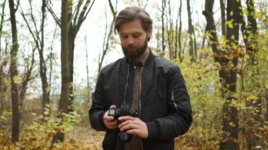 Elinde kamerayla sonbahar ormanında yürüyen ve altın sonbaharın manzaralarını fotoğraflayan vahşi bir fotoğrafçının portresi.