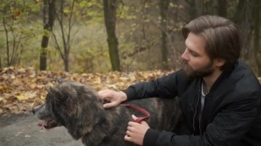 Sonbahar parkında köpeği gezdiren beyaz bir adam. Köpeği sev ve ona bak.