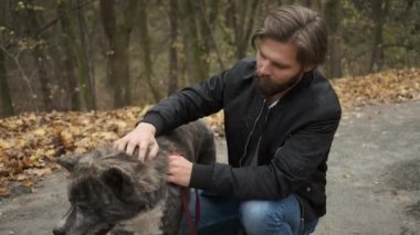 Sonbahar parkında köpeği gezdiren beyaz bir adam. Köpeği sev ve ona bak.