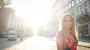 Güzel sarışın, beyaz tenli, samimi bir gülüşü ve güzel, uzun bir elbisesi var. Sabah kentinde kasıla kasıla yürüyor. Kameranın önünde poz vermek. Model