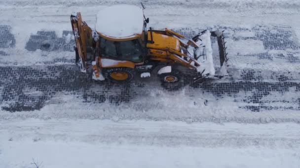 Una excavadora amarilla desplaza la carretera desde la nieve. Mal tiempo para despejar carreteras por servicio de carretera. Marco desde arriba — Vídeo de stock