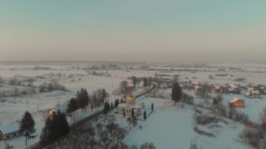 Ukrayna 'nın karla kaplı köyünün üzerinde İHA uçuşu. Bir kış masalı. Soğuk kışta gün batımı
