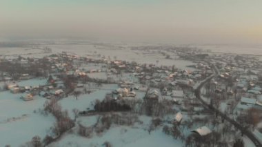 Ukrayna 'nın karla kaplı köyünün üzerinde İHA uçuşu. Bir kış masalı. Soğuk kışta gün batımı