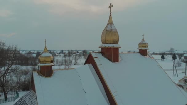 Lot dronem nad kościołem z widokiem na wioskę pokryty jest śniegiem. Zimowa bajka — Wideo stockowe