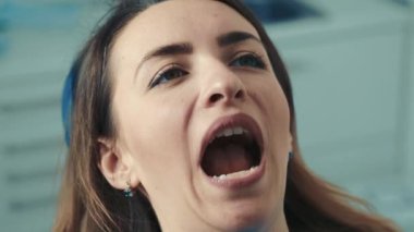 30 yaşında, gözlüklü bir erkek dişçi, dişçi koltuğunda oturan beyaz görünümlü bir kızın dişlerini tedavi ediyor. Sağlıklı bir gülümseme