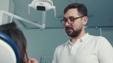 Kafkas görünümlü bir dişçi, yüz dişçi koltuğundaki bir hastayla iletişim kurar.